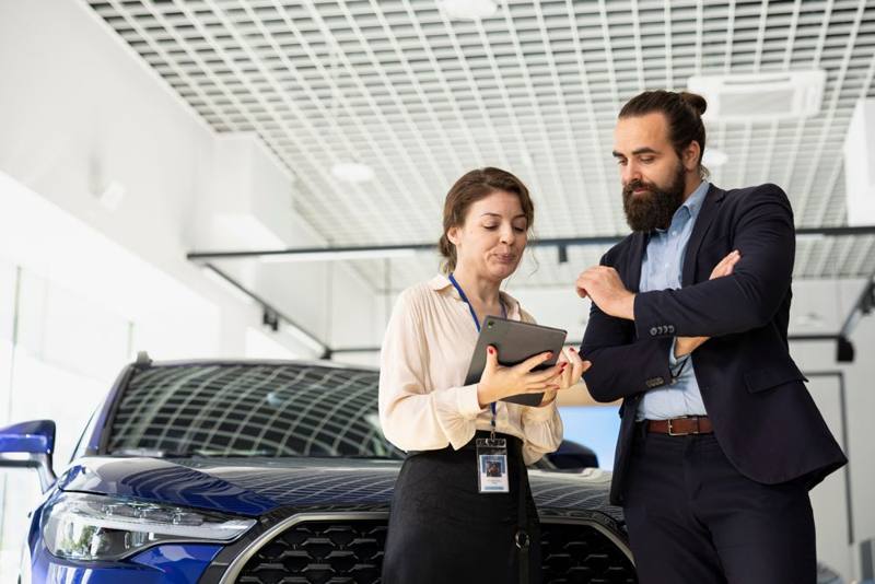 Professionisti di una concessionaria consultano una pratica accanto a un'auto
